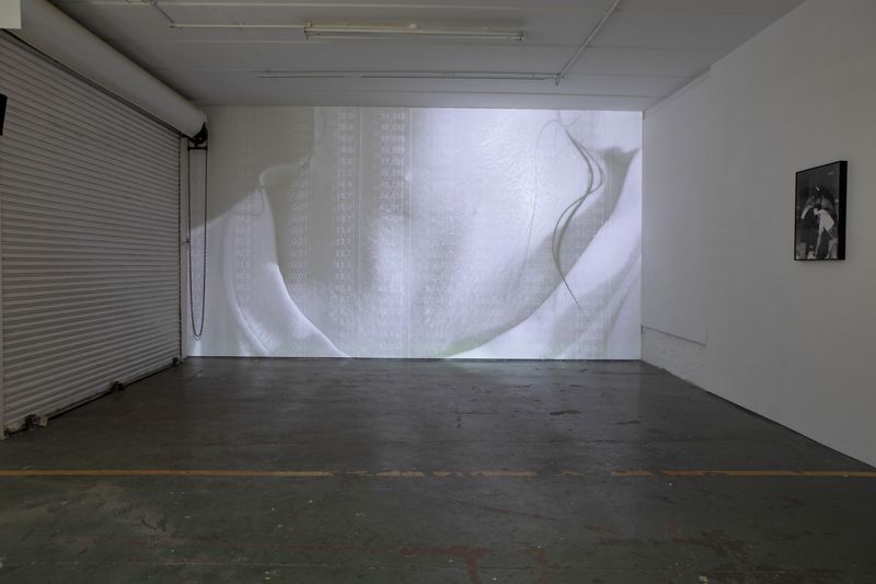 Large projection on backwall of gallery space close up image of woman's neck sweating film by Yasmin Vardi